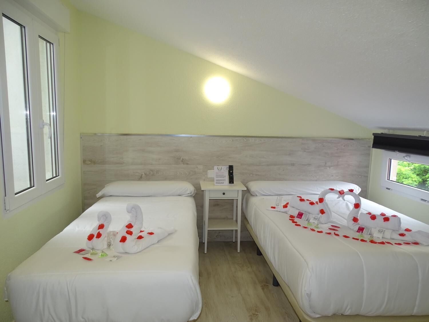 Habitación de hotel con dos camas, cada una decorada con toallas y pétalos de rosa.