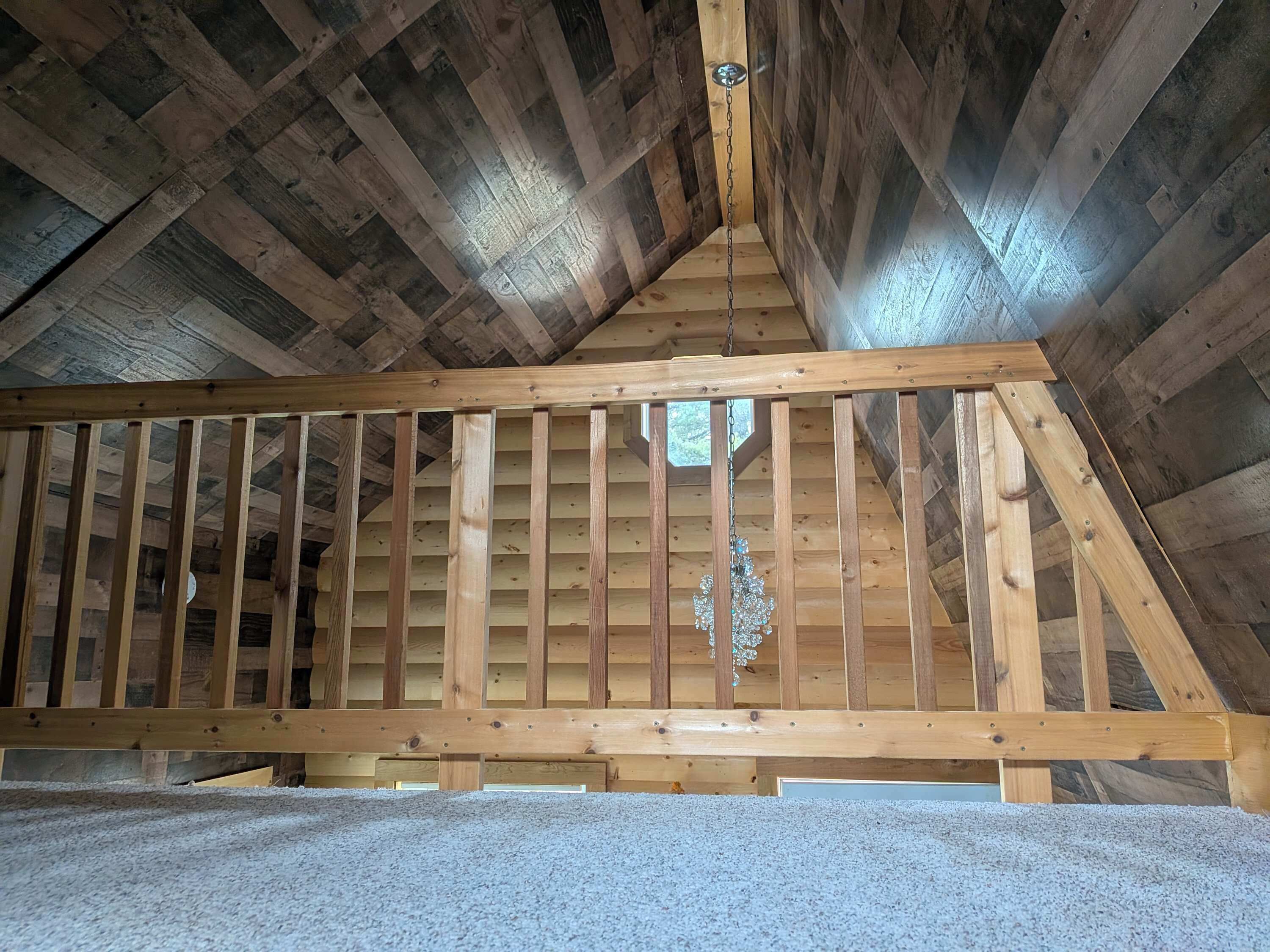 A wooden ceiling with a sloped design, a wooden beam structure, and a hanging light fixture.