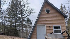 A log cabin with a white door, a small window, and a wooden deck leading to the entrance.