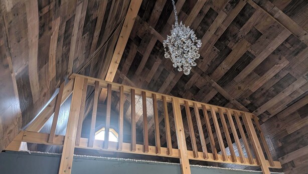 A wooden balcony with a metal railing, a chandelier, and a window.