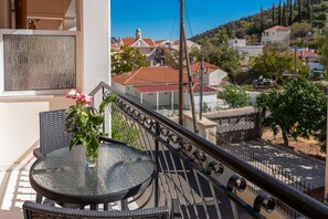 Un balcón con una mesa y sillas de vidrio, un jarrón con flores y vistas a una zona residencial con casas y árboles.