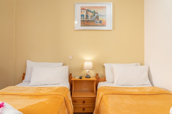 Habitación de hotel con dos camas, una mesita de noche con lámpara, un cuadro en la pared y un cajón de madera.