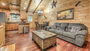A cozy cabin interior with wooden walls, a dining area, and a living room with a sofa and coffee table. - Colby's Cabin- Pet Friendly | Creek Access | Screened Porch (Blue Ridge)