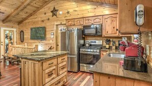 A wooden cabin interior with a kitchen featuring a refrigerator, microwave, stove, and sink. - Colby's Cabin- Pet Friendly | Creek Access | Screened Porch (Blue Ridge)