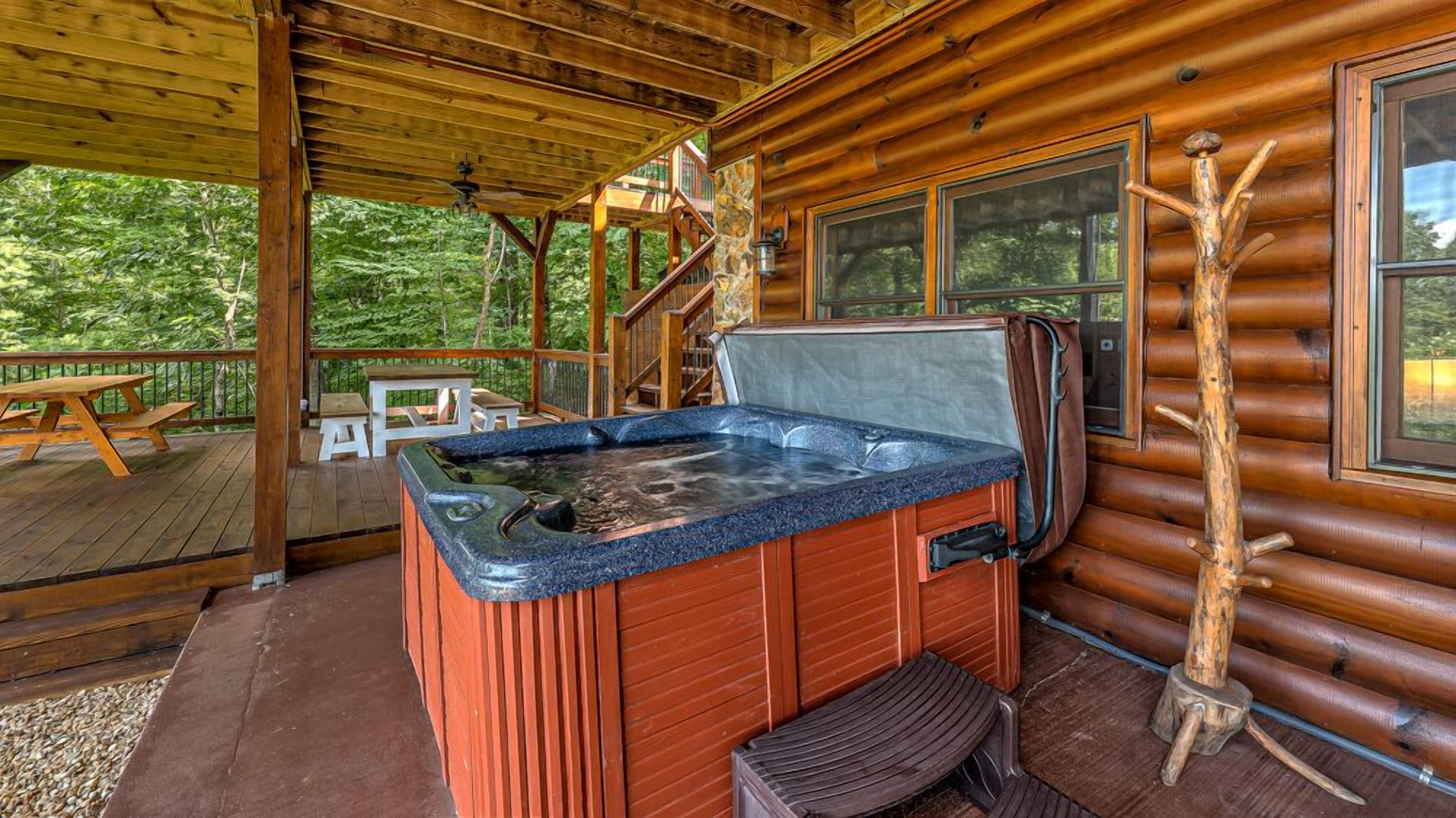 En træhytte med jacuzzi, træterrasse og en stenvæg.
