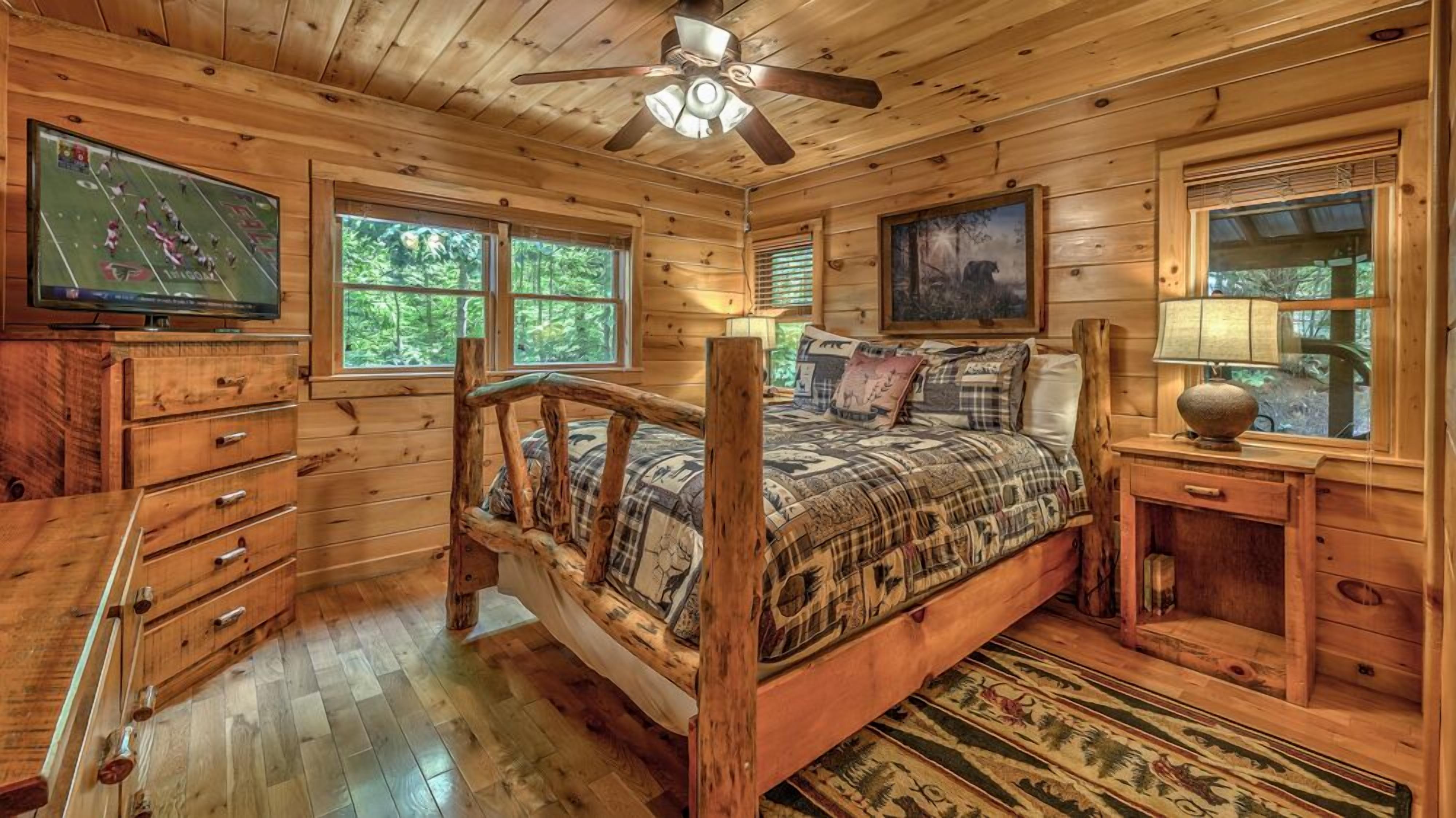 A wooden cabin room with a bed, a television, a desk, and a window.