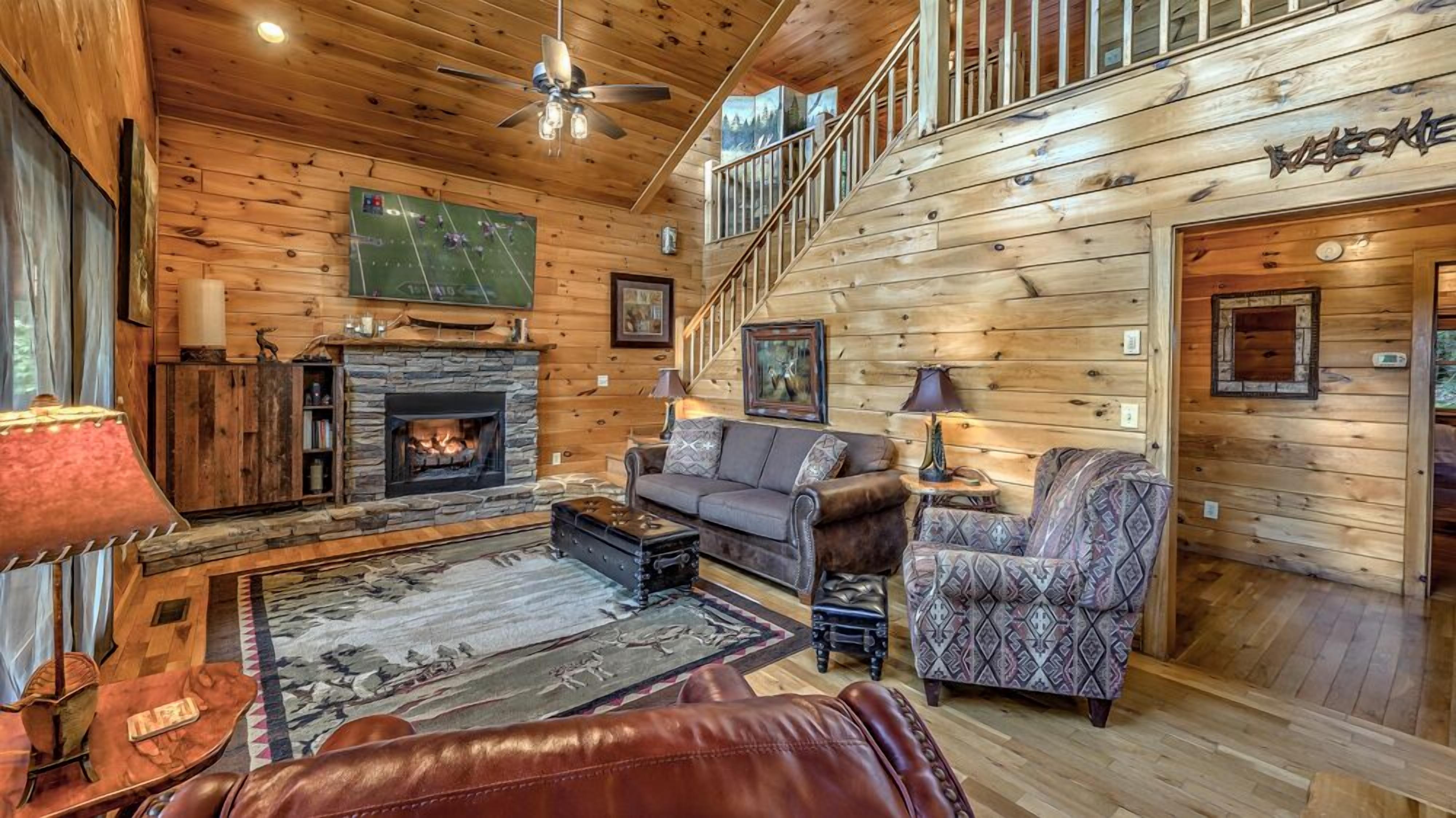 L’intérieur chaleureux d’un chalet en bois comprend une cheminée, un canapé, un fauteuil à motifs et un escalier menant à un étage supérieur.