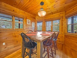 Een houten cabin met een eetgedeelte, een grote tafel, stoelen en een hanglamp.