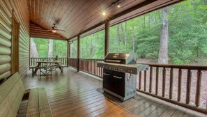 Een overdekt terras met een barbecue en picknicktafel, omgeven door een houten balustrade en uitzicht op het bos.