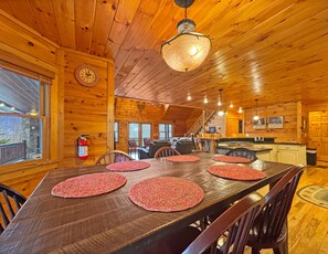 A wooden cabin interior with a dining table, chairs, a bar area, and a staircase. - Laurel Valley Lodge- Pet Friendly | Outdoor Fire Pit & Fireplace | Game Room (Blue Ridge)