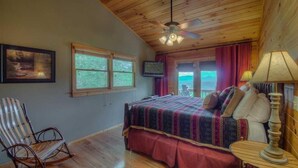 A bedroom with a bed, a chair, a television, and a window with a view. - Heavens Whisper- Lake and Mountain Views | Outdoor Fire Pit | Aska Adventure Area (Blue Ridge)