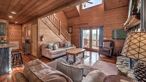A cozy log cabin interior with a wooden staircase, a sofa, a coffee table, and a fireplace. - Daze Off- Spectacular Views | Large Hot Tub | Outdoor Fire Pit (Morganton)