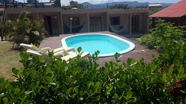 A swimming pool with a wooden deck, lounge chairs, and a view of mountains in the background. - Cabanas Canto Livre (Imbituba)