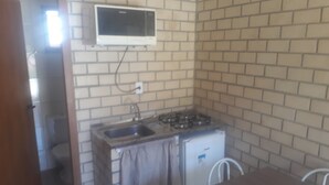 A compact kitchen with a gas stove, sink, and a microwave. - Cabanas Canto Livre (Imbituba)