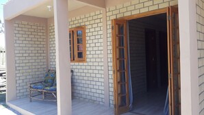 A covered porch with a chair, a wooden door, and a window. - Cabanas Canto Livre (Imbituba)