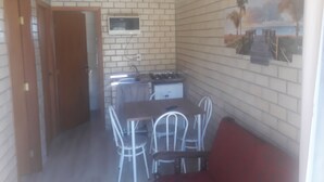 A compact kitchen with a microwave, stove, and sink, a dining area with metal chairs, and a brick wall with a painting. - Cabanas Canto Livre (Imbituba)