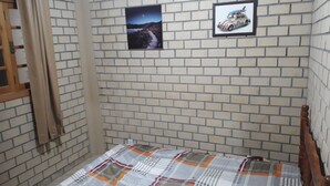 A small, narrow room with a brick-patterned wall, a bed with a plaid bedspread, and two framed pictures. - Cabanas Canto Livre (Imbituba)