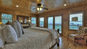 A wooden cabin bedroom with a large bed, a chair, and a ceiling fan.