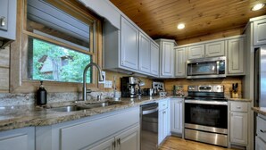 A modern kitchen with white cabinets, stainless steel appliances, a granite countertop, and a wooden ceiling.