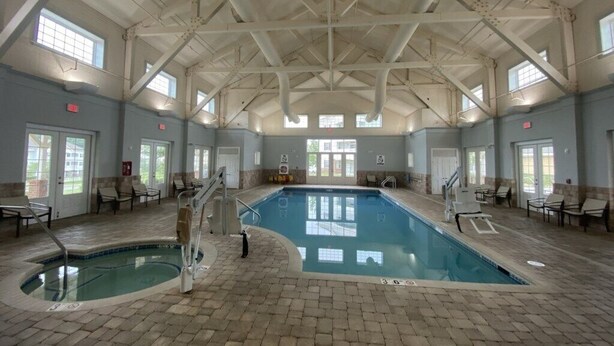 Una piscina interior con suelo de baldosas, un trampolín y sillones de descanso alrededor de la zona de la piscina.