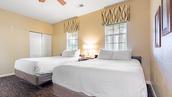 A hotel room with two beds, a desk, a lamp, and a window with curtains.