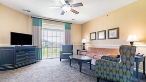 Une chambre d’hôtel équipée d’une télévision, d’un canapé, d’un fauteuil à motifs, d’une table basse et d’un ventilateur de plafond.