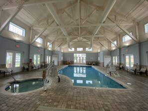 Ein Hallenbad mit Fliesenboden, Sprungbrett und Liegestühlen rund um den Poolbereich.