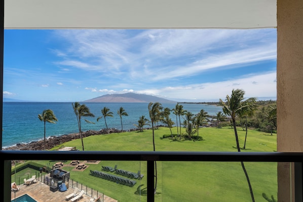 A view from a window overlooking a golf course with a beach and ocean in the background.