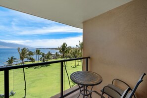 A balcony with a view of a green lawn, palm trees, and a body of water. - Kihei Surfside #608: Oceanfront Sanctuary with Spectacular Views! (Kihei, Maui)