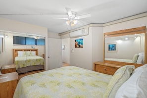 A bedroom with two beds, a ceiling fan, a large mirror, and a window with blinds.