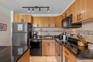 A modern kitchen with wooden cabinets, stainless steel appliances, and a granite countertop. - Kihei Surfside #608: Oceanfront Sanctuary with Spectacular Views! (Kihei, Maui)