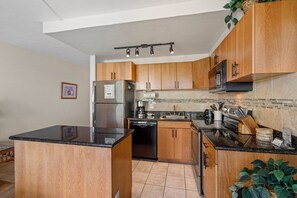 Eine Küche mit Holzausstattung, einer schwarzen Arbeitsplatte, einem Edelstahlkühlschrank und einer Mikrowelle.