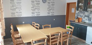 Un coin repas avec une table et des chaises, une cuisine équipée de placards et un mur sur lequel sont inscrits des noms de villes.