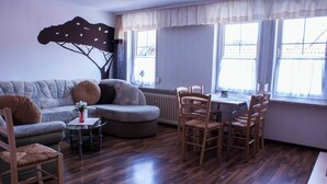 Un salon comprenant un canapé, des fauteuils, une table basse et une table à manger avec des chaises.