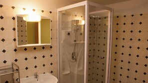 Een badkamer met een douchecabine van glas, een wastafel en een spiegel met verlichting erboven.