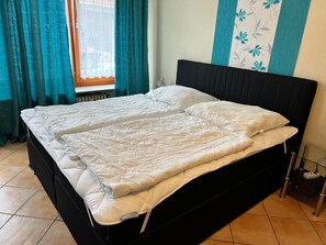 Un lit double avec une tête de lit noire, du linge de lit blanc et une fenêtre avec des rideaux.