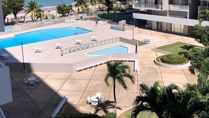 Un área de piscina de hotel con múltiples piscinas, sillas de descanso y palmeras.