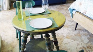 Una sala de estar con un sofá azul, una mesa de comedor con platos y vasos, un ventilador de techo y una pequeña planta en la pared.