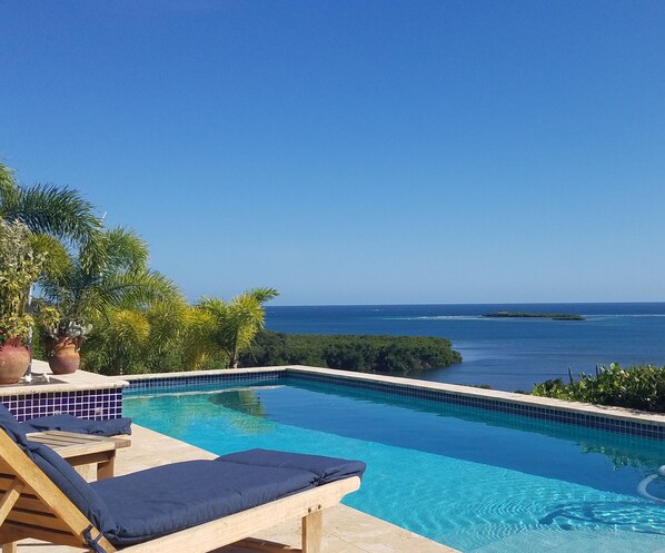 A clear blue sky, a swimming pool with lounge chairs, and a view of the ocean.