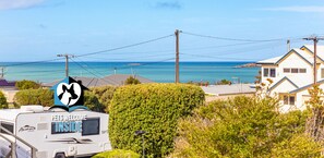 A caravan with a 'PETS WELCOME INSIDE' sign, surrounded by greenery and overlooking a coastal area with houses and a clear sky. - 18 Dundalk Ave, McCracken - Contemporary 3 Bed 2 Bath Home with Ocean View & Wi-Fi (McCracken)