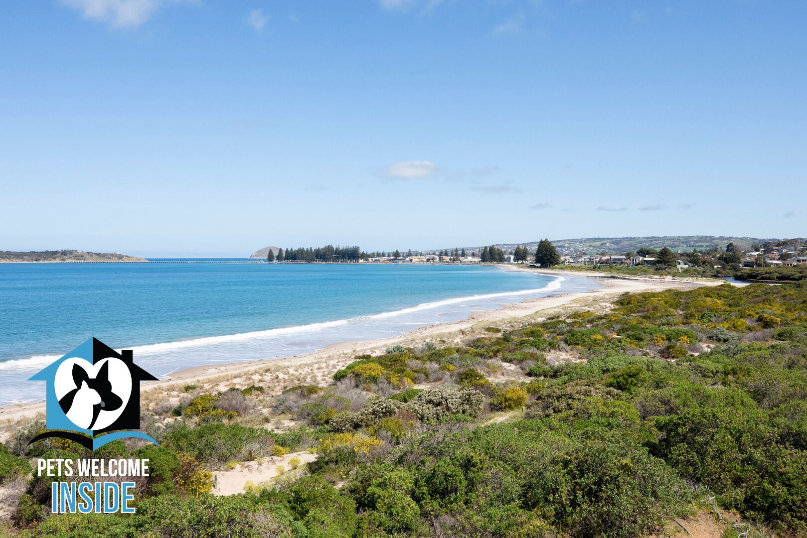 A coastal landscape with a beach, dense greenery, and a clear blue sky.