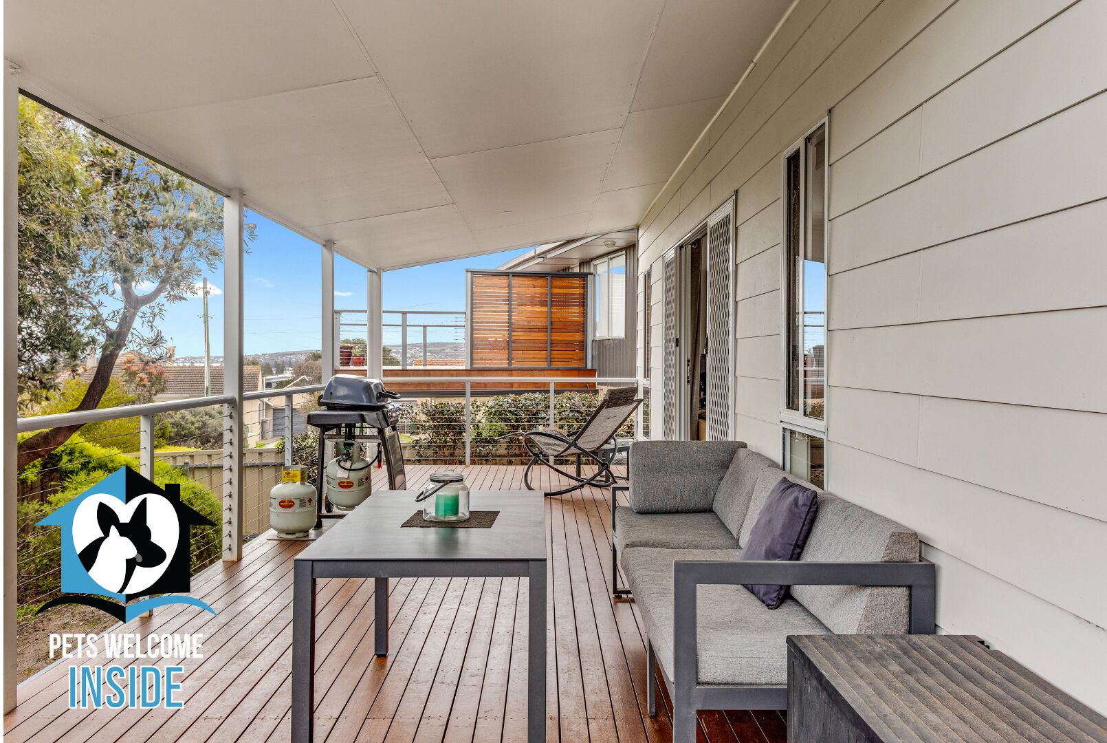 A covered outdoor patio with a sofa, a table, and a grill.