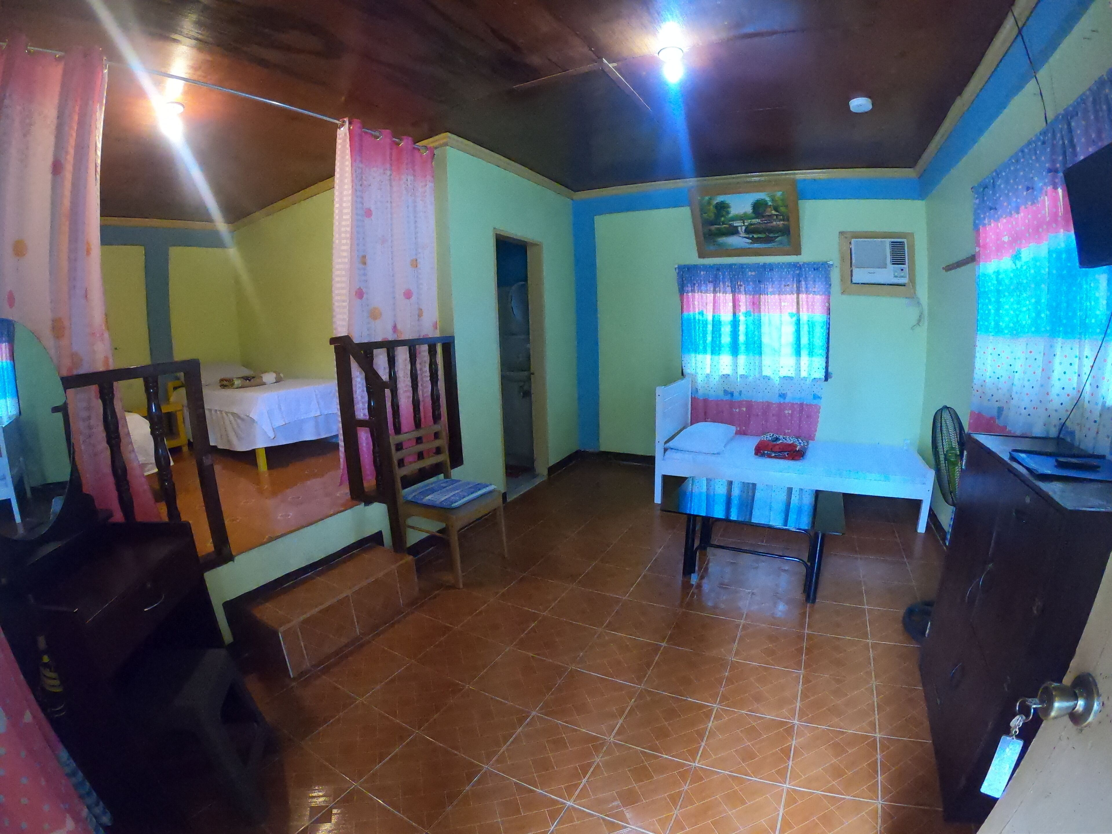 A room with a bed, a chair, a table, and a fan.