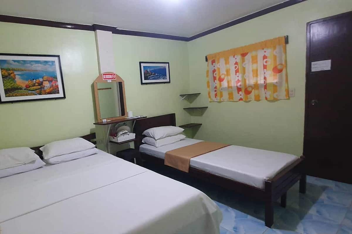 Une chambre avec deux lits, un miroir, une étagère avec une tasse et deux tableaux encadrés au mur.