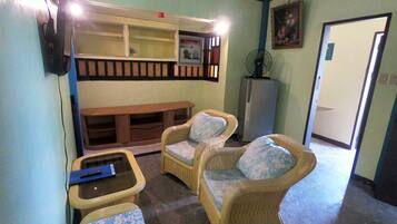 Una habitación con muebles de mimbre, un banco, una mesita y un refrigerador.