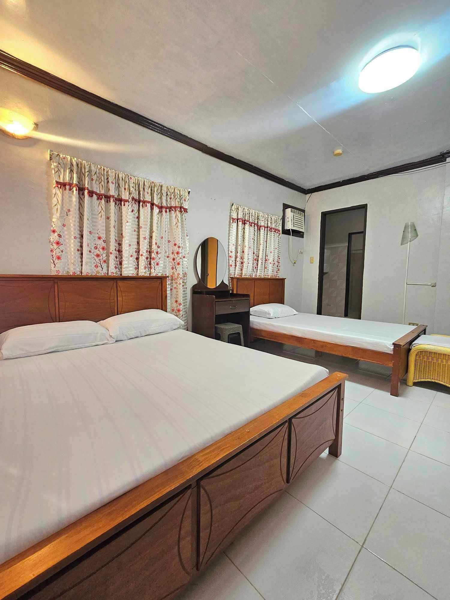 A hotel room with two single beds, a wooden headboard, a small desk with a mirror, and a wardrobe.