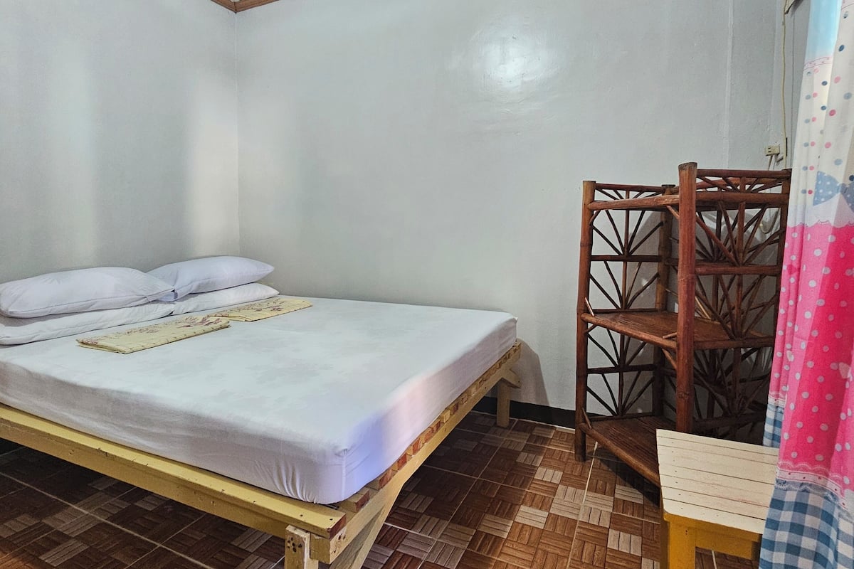 Une petite pièce, bien rangée, avec un lit simple, une chaise en bois et un rideau à motifs.