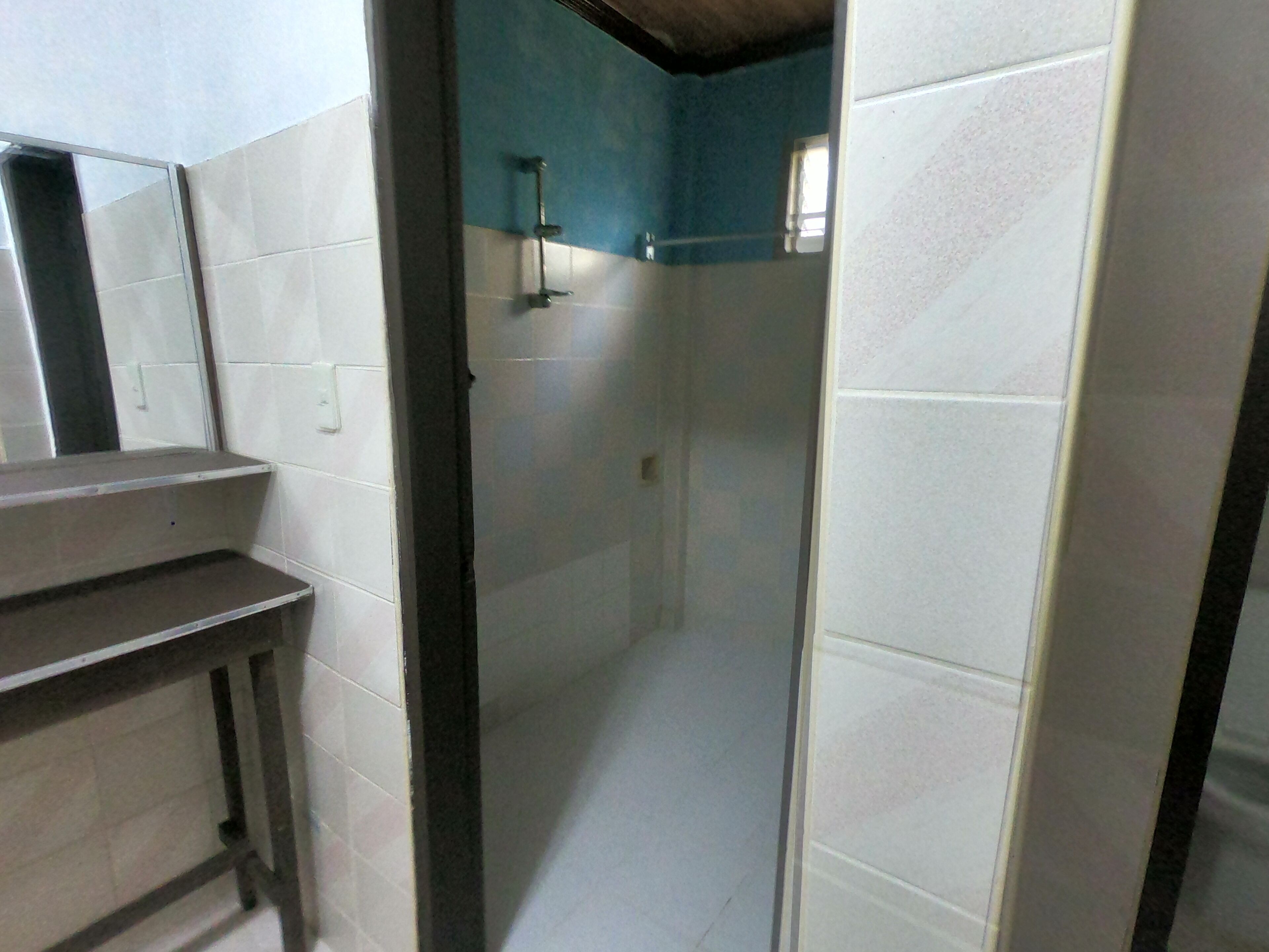 A bathroom with white tiled walls, a dark wooden bench, and a shower area with a blue accent wall.