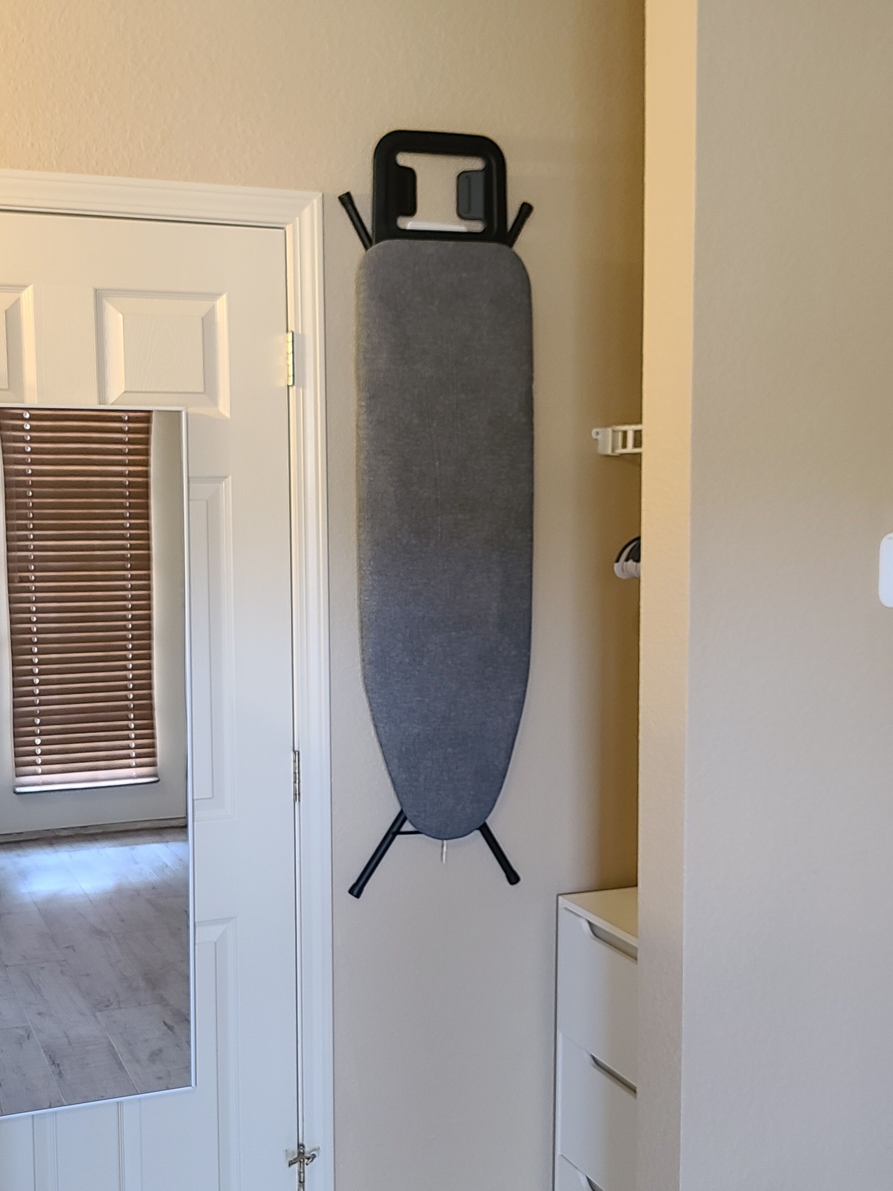 A room with a door, a window with blinds, and a wall-mounted ironing board.
