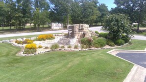A stone structure surrounded by well-maintained landscaping, including a grassy area and yellow flowers. - One bedroom resort condo on Golf Course with pool. 10 minutes to SDC! (Branson West)
